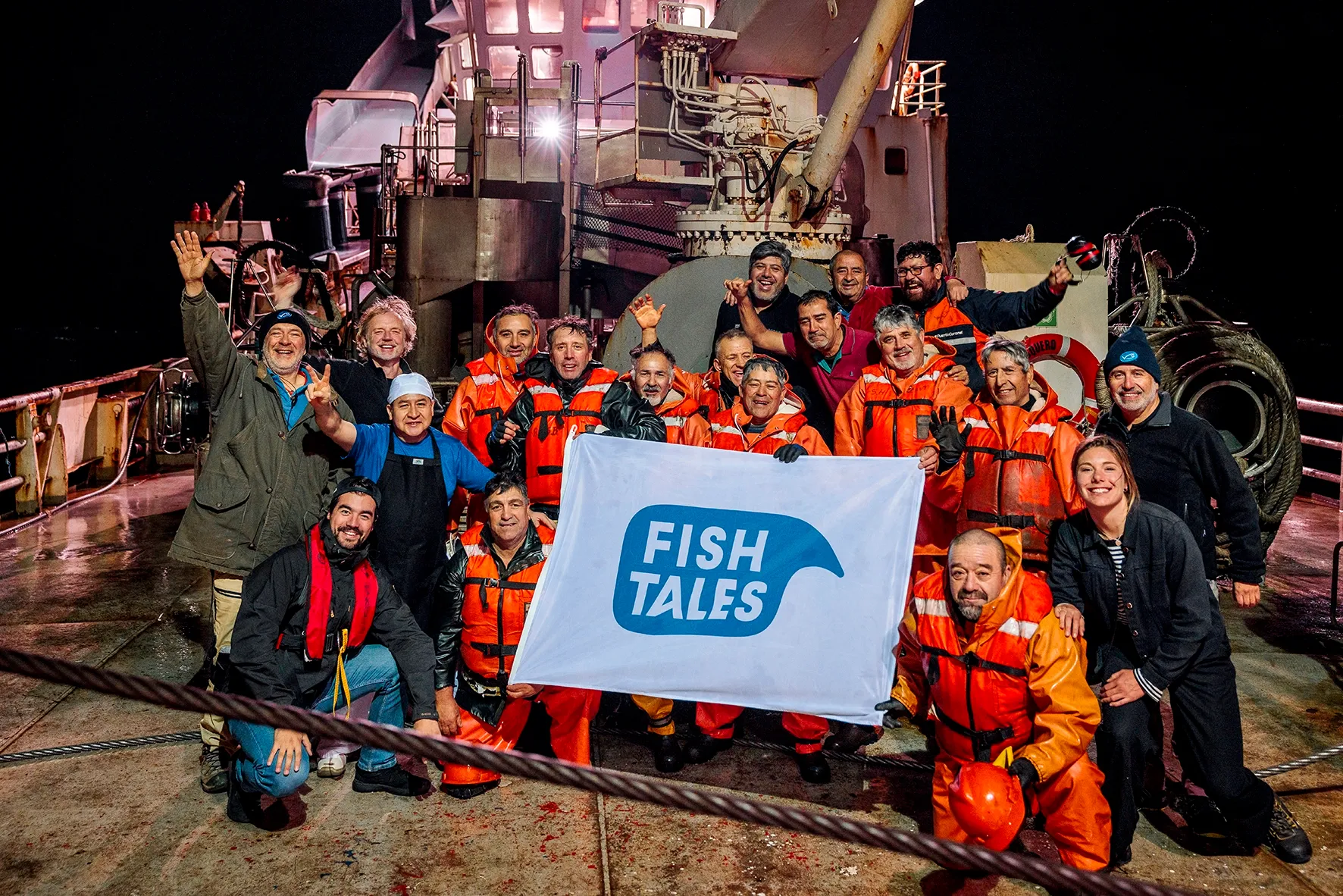 Groepsfoto vissers aan boord in Chili met Fish Tales vlag.