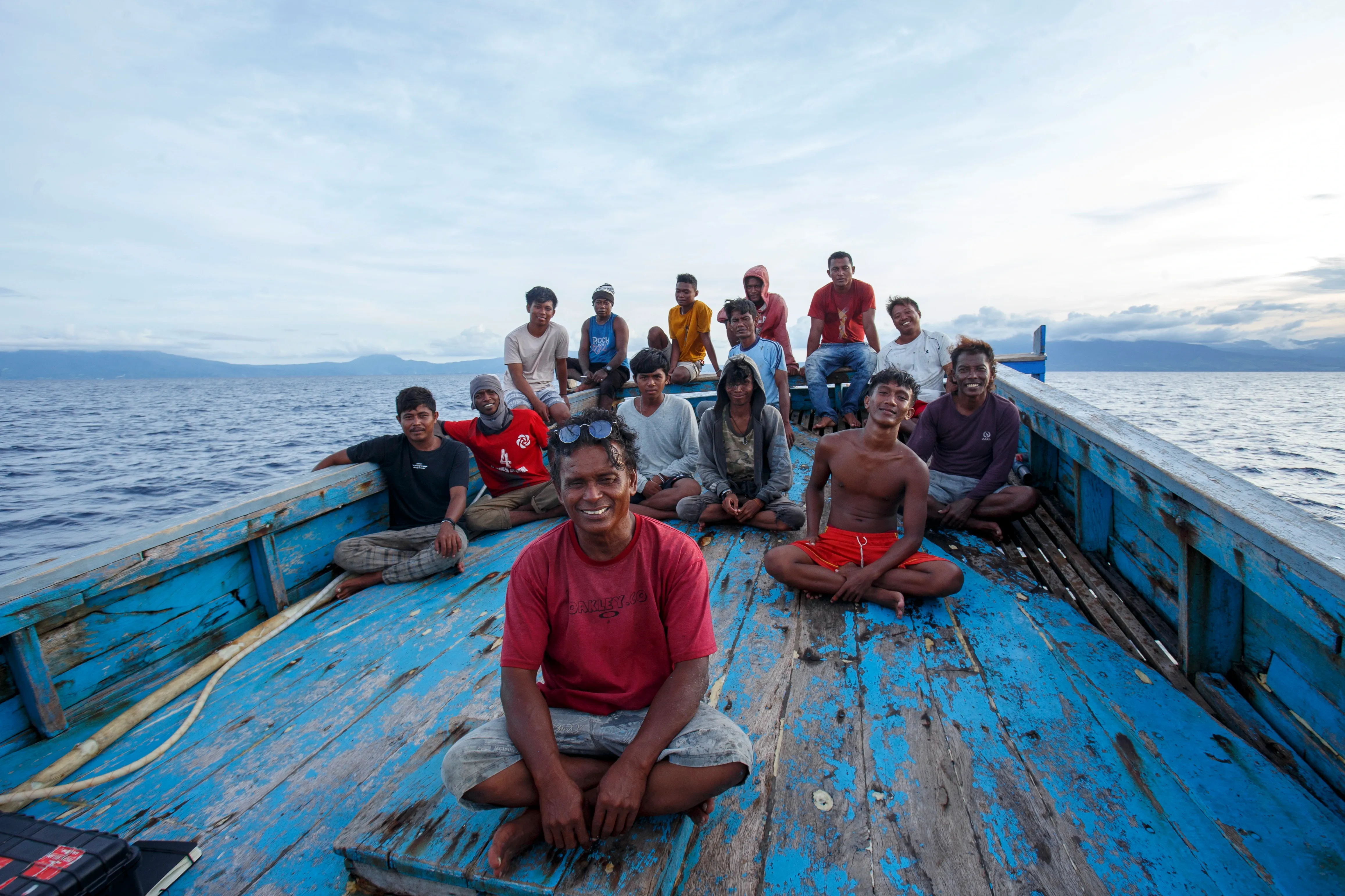 Group of smiling people sitting on a blue wooden boat on a lake.