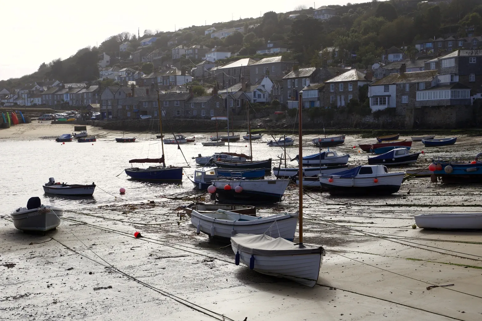 Boats rest on mudflats in a sunlit harbor, a village rising on the distant hill.