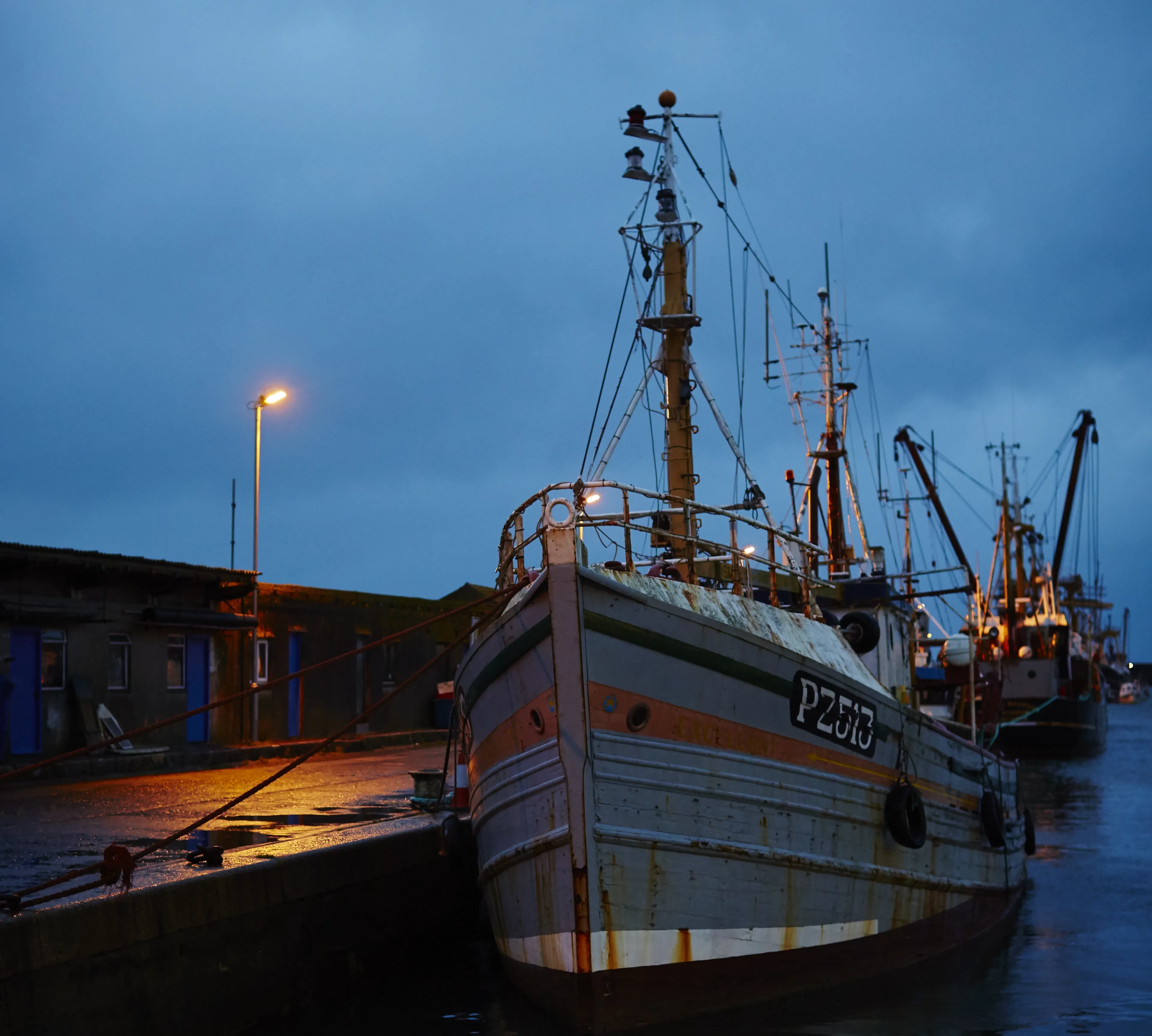 Fishing boat PZ21 docked at a pier under a dark blue evening sky.